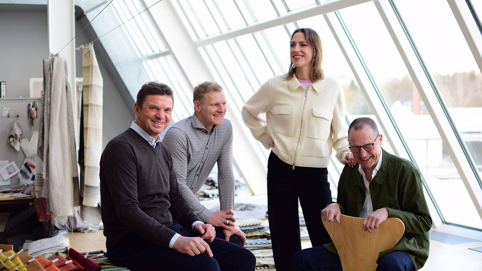 Team von Stoffexperten in modernem Atelier mit Stoffmustern und großen Fenstern bei gemeinsamer Besprechung.