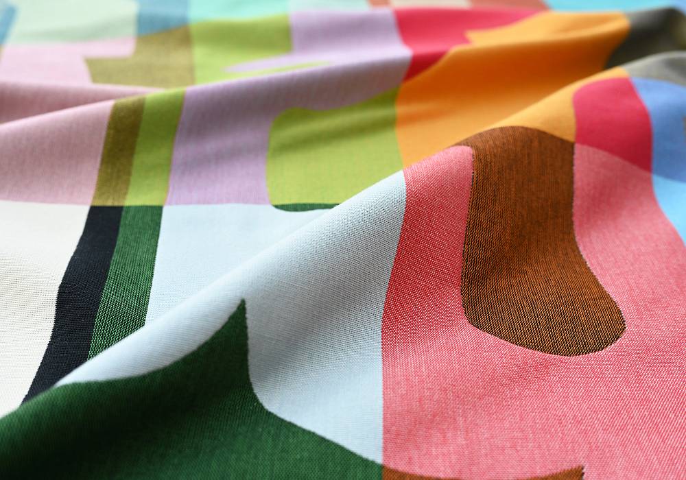 Bunter Designstoff mit abstrakten Formen und kräftigen Farben, weich fallend mit sichtbarer Textilstruktur.